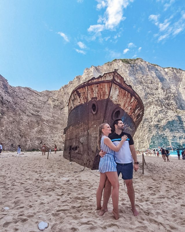 Couple posing in front of the Shipwreck at the Shipwreck Beach / Navagio Beach in Zakynthos (Greece)