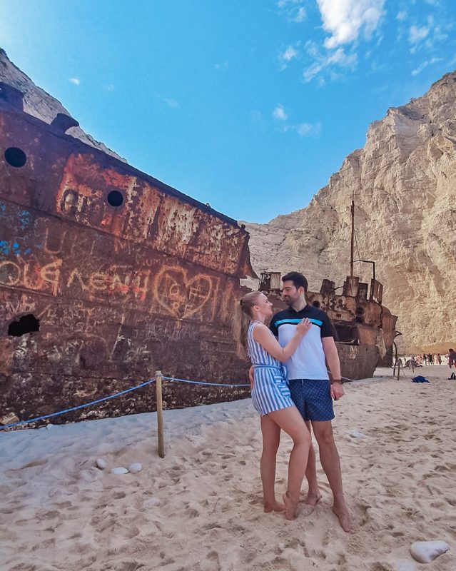 Couple posing in front of the Shipwreck at the Shipwreck Beach / Navagio Beach in Zakynthos (Greece)