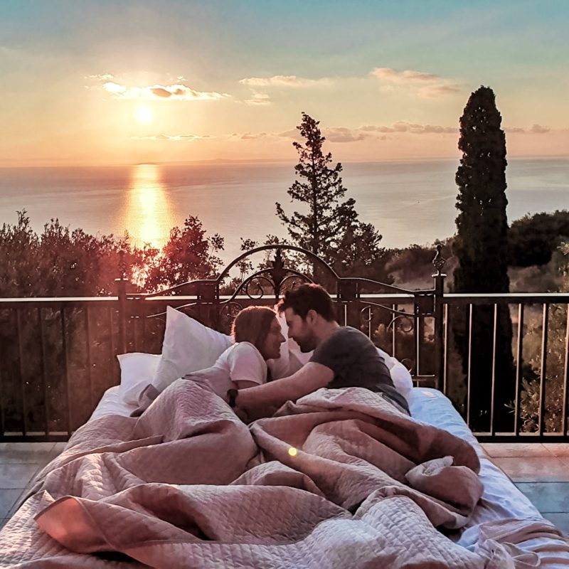 Travel Couple enjoying the sunrise from bed at Armyra Villas in Zakynthos (Greece)