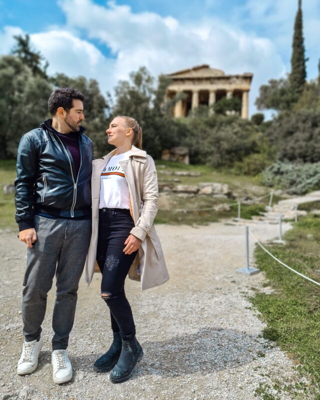 Travel Couple posing in front of the Temple of Hephaestus at the Ancient Agora of Athens, Greece