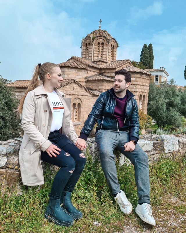 Travel Couple posing in front of the Church of the Holy Apostles at the Ancient Agora of Athens, Greece