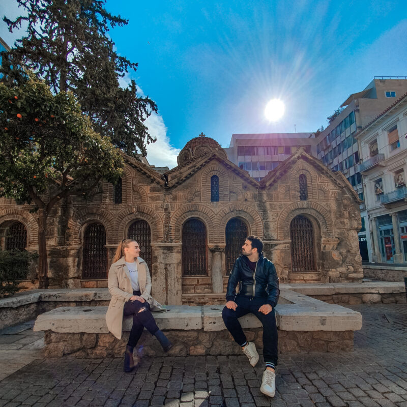 Travel couple posing in front of Panagia Kapnikarea church in Athens, Greece