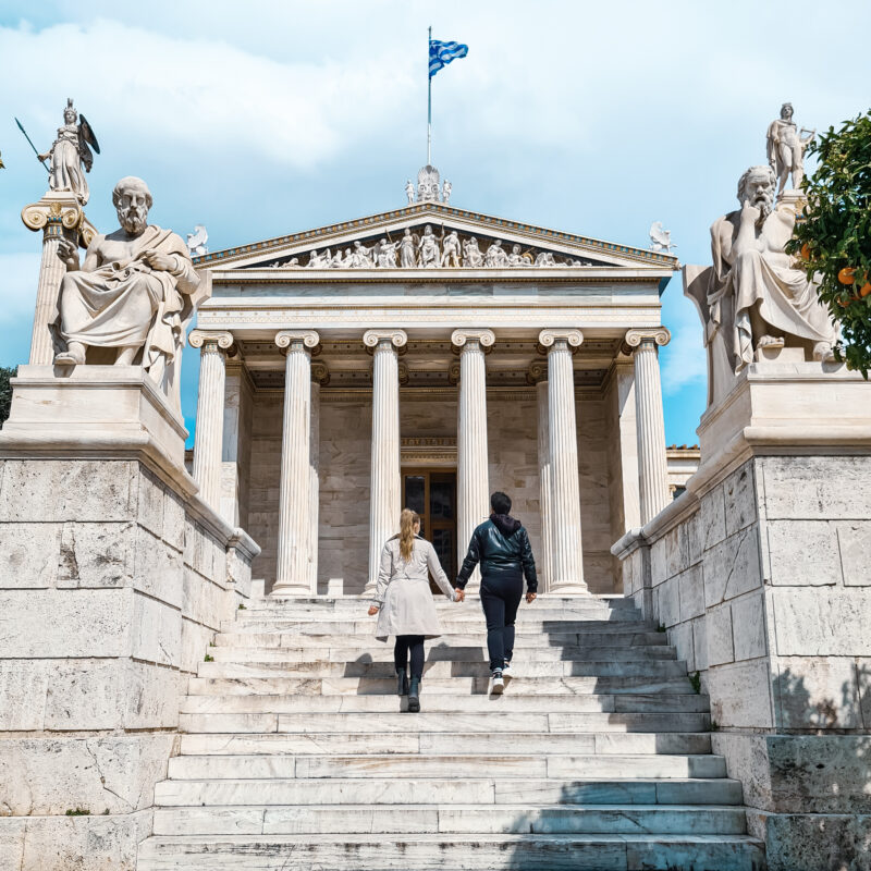 Travel couple posing in front of Academy of Athens, Greece