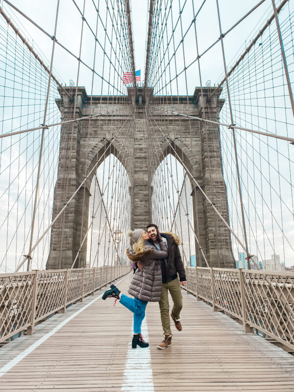 Travel couple crossing the iconic Brooklyn Bridge in New York City