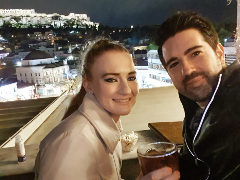 Couple enjoying a cocktail at a rooftop bar in Athens with Acropolis views at night