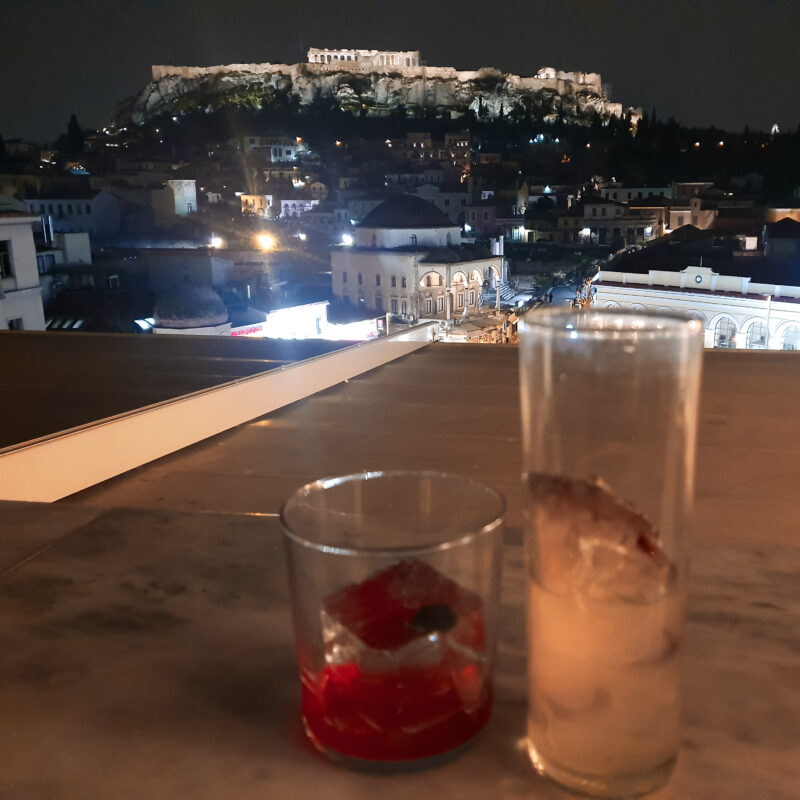 Couple enjoying a cocktail at a rooftop bar in Athens with Acropolis views at night