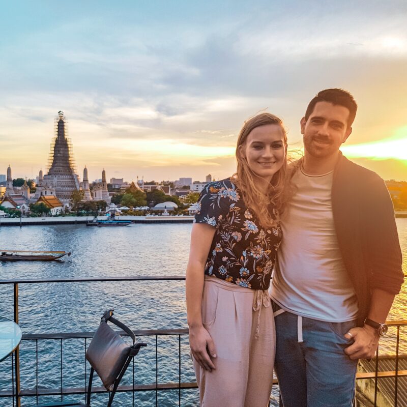 Travel couple watching the sun set over Wat Arun in Bangkok, Thailand