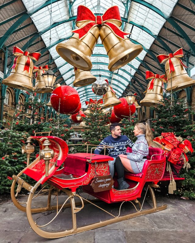 Travel Couple posing with the Santa Sleigh Christmas Display in Covent Garden, London