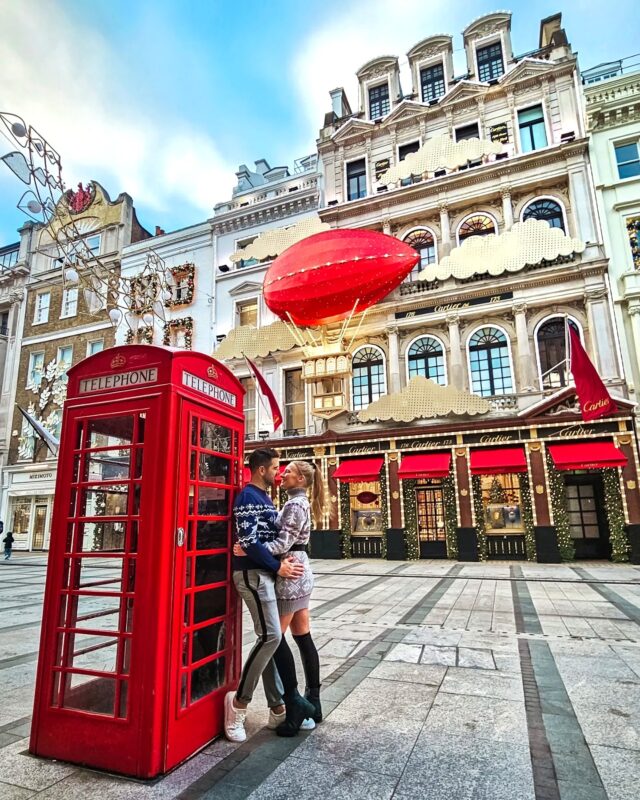 Travel Couple posing with Christmas Decorations and iconic red phone booth at the Cartier store in New Bond Street London